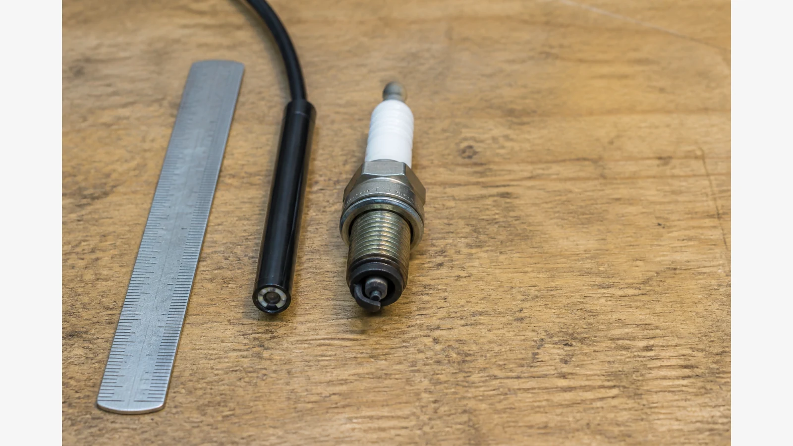 Slim inspection camera probe tip next to a spark plug on a UK garage workbench